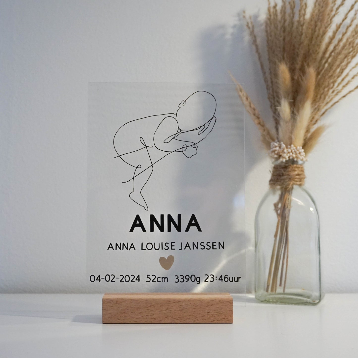 Een transparant acrylglas frame met een gepersonaliseerde line art illustratie van een baby op een arm.