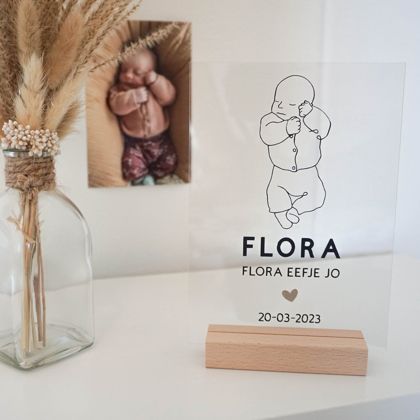 Een houten frame met een acrylplaat waarop een line art tekening van een baby is afgebeeld, samen met de naam en geboortedatum.