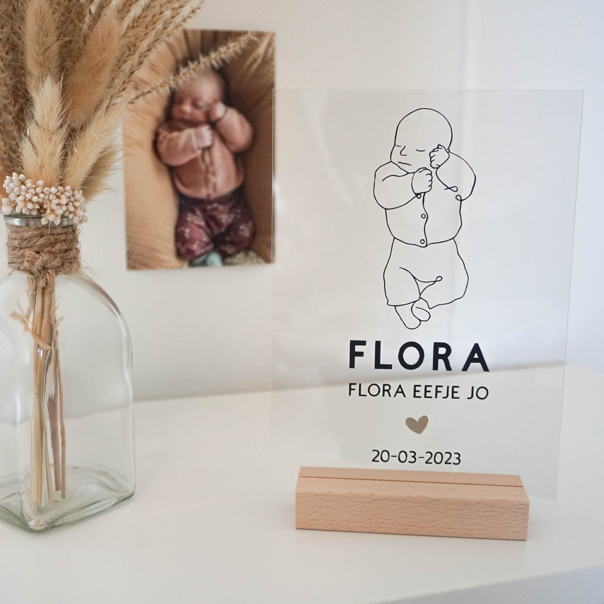 Een houten frame met een acrylplaat waarop een line art tekening van een baby is afgebeeld, samen met de naam en geboortedatum.