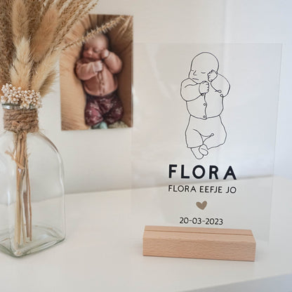 Een houten frame met een acrylplaat waarop een line art tekening van een baby is afgebeeld, samen met de naam en geboortedatum.